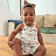 Alina a rejoint le concours — aidez-le/la à gagner de superbes lots ! toddler, child, baby, table, romper, headband, bow, smile, face, living_room, couch, furniture, wood, curly_hair, skin, indoors, cute, sitting, person, happy
