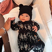Kai joined the competition — help win amazing prizes! baby, infant, child, onesie, skeleton_pattern, black_hat, bear_ears, hand_holding, changing_pad, soft_toys, basket, pink_cloth, wooden_surface, indoor, cute, portrait, person, clothing, newborn, cozy