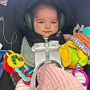 Kai joined the competition — help win amazing prizes! baby, car_seat, child, ear_protectors, toy, blanket, safety_harness, infant, seatbelt, colorful, striped_clothing, smiling, indoor, person, cute, comfort, head_support, plaything, soft_toy, secure