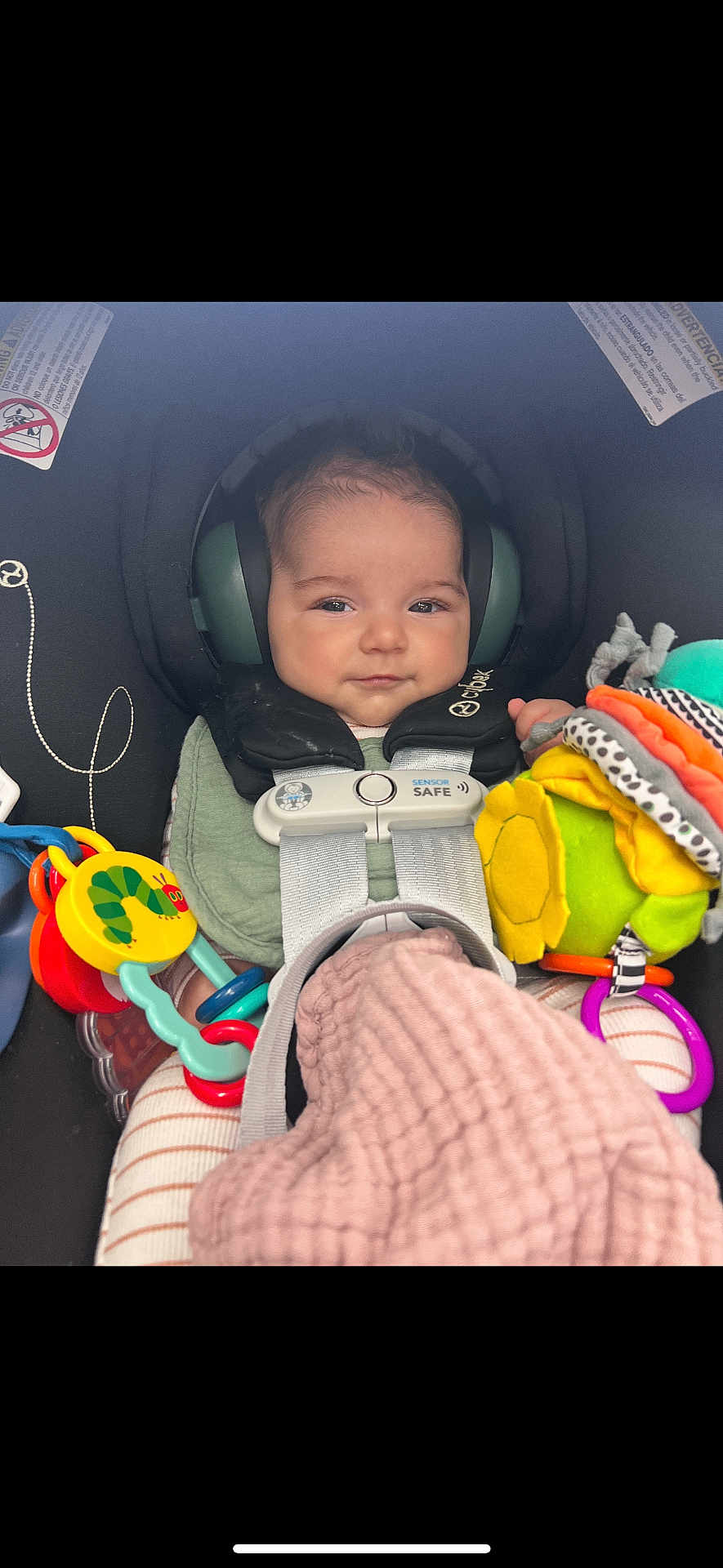 Kai joined the competition — help win amazing prizes! baby, car_seat, child, ear_protectors, toy, blanket, safety_harness, infant, seatbelt, colorful, striped_clothing, smiling, indoor, person, cute, comfort, head_support, plaything, soft_toy, secure