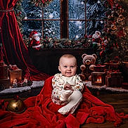 Leo joined the competition — help win amazing prizes! baby, child, christmas, holiday, festive, pajamas, red_blanket, teddy_bear, gifts, candles, snow, window, curtains, floor, wooden_floor, decorations, christmas_tree, ornaments, santa_dolls, smiling