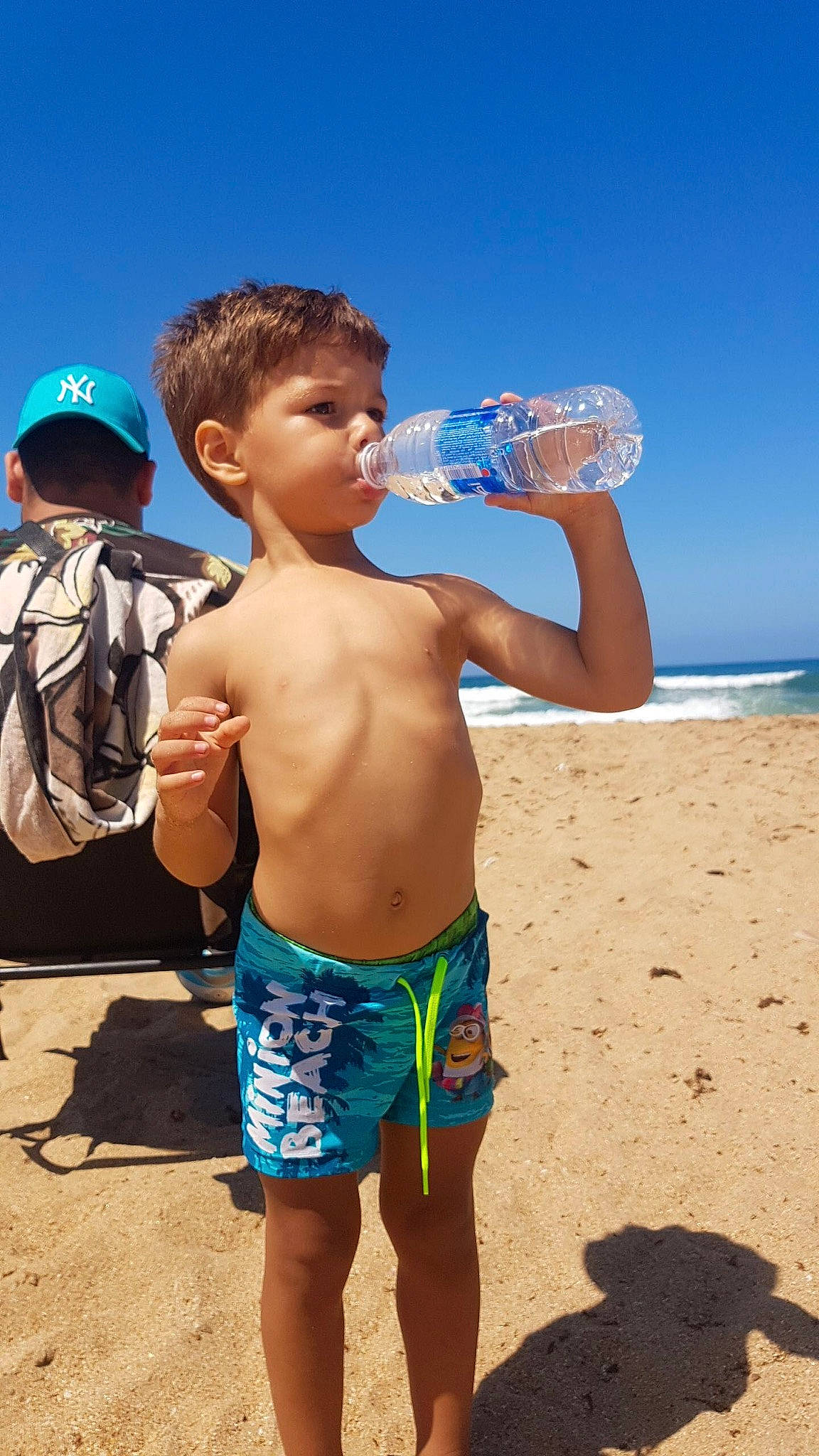 Zyad participe au concours pour gagner de l'argent avec cette photo : barechested, beach, board_short, child, drink, drinking, drinking_water, fun, muscle, person, plastic_bottle, play, shorts, summer, toddler, trunks, vacation, water, water_bottle