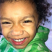 King is registered to the contest to win money with this photo: child, smiling, close_up, face, curly_hair, green_hoodie, happy, joyful, casual_clothing, portrait, cute, person, expression, young, indoors, sweatshirt, teeth, skin, eyelashes, nostrils