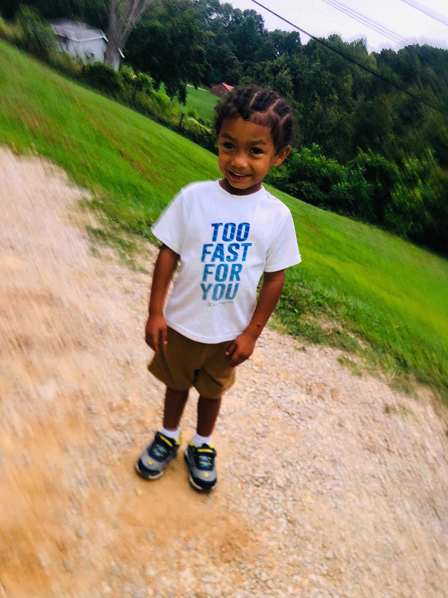 King is registered to the contest to win money with this photo: child, boy, outdoor, grass, trees, gravel, tshirt, shorts, sneakers, smiling, braids, person, nature, greenery, casual, standing, daylight, young, happy, portrait