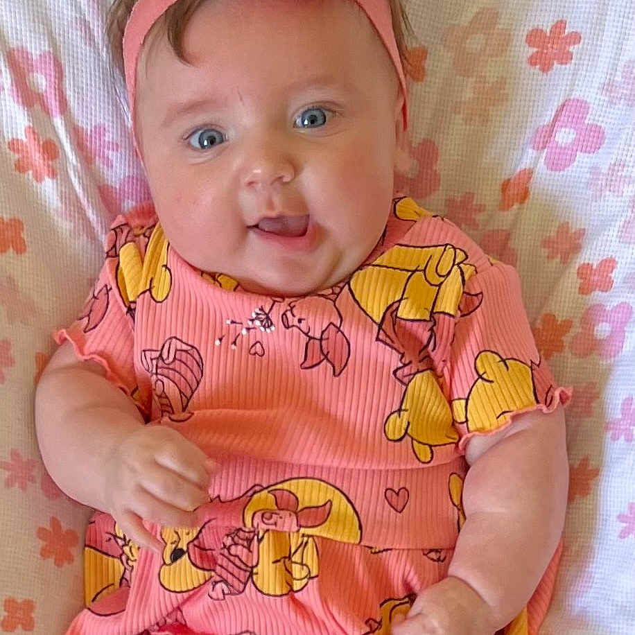 Ava is registered to the contest to win money with this photo: baby, babylaughing, clothing, cushion, face, flower, furniture, happy, hat, head, newborn, person, photography, plant, portrait, rose, sitting, sleeve, smile, t_shirt