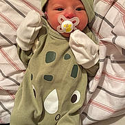 Saturn is registered to the contest to win money with this photo: baby, newborn, pacifier, mittens, hat, green_outfit, rhino_design, striped_blanket, lying_down, infant, sleepwear, cute, small, child, person, cozy, soft, indoor, resting, wearing