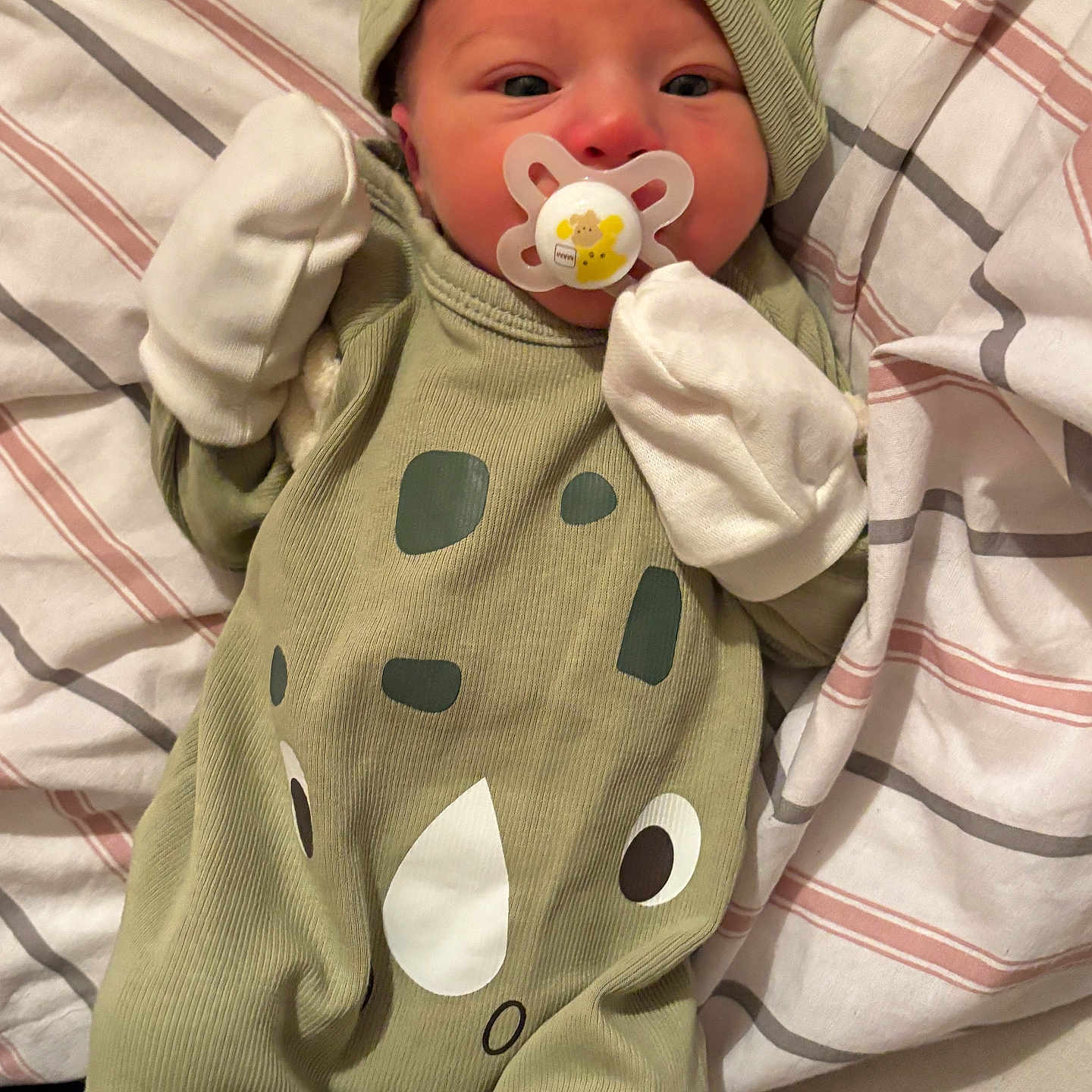 Saturn is registered to the contest to win money with this photo: baby, child, cozy, cute, green_outfit, hat, indoor, infant, lying_down, mittens, newborn, pacifier, person, resting, rhino_design, sleepwear, small, soft, striped_blanket, wearing