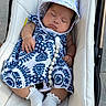 baby, sleeping, stroller, dress, hat, white_socks, pacifier, bead_chain, cushion, infant, peaceful, child, outdoor, blue_and_white, patterned_clothing, hand, footwear, closeup, cute, resting