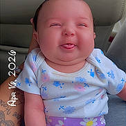 Aliyah joined the competition — help win amazing prizes! baby, child, tongue_out, smiling, floral_clothing, purple_shorts, white_shirt, car_seat, tattooed_arm, hand, infant, cute, portrait, indoors, person, seat, holding, playful, expression, date_stamp