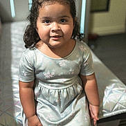 Emily is registered to the contest to win money with this photo: child, girl, toddler, portrait, smiling, sitting, bedroom, bed, floral_dress, hair_bows, curly_hair, indoors, face, eyes, clothing, furniture, home, natural_light, photography, happy