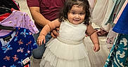Emily joined the competition — help win amazing prizes! child, toddler, adult, father, daughter, smiling, dress, white_dress, bow, fashion, clothing_store, clothing_racks, shopping, portrait, family, indoor, standing, sitting, accessories, happy