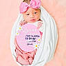 baby, newborn, infant, pink_bow, blanket, swaddled, portrait, cute, soft_background, sign, birth_details, feet, hands, headband, child, lying_down, person, studio_photo, pink, white