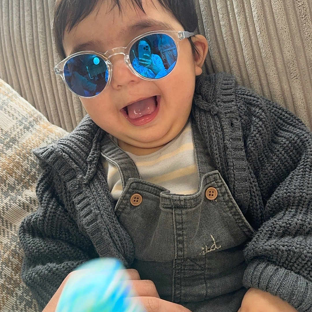 Haleefa joined the competition — help win amazing prizes! accessories, baby, clothing, coat, couch, face, furniture, glasses, happy, hat, head, jacket, knitwear, pants, person, photography, portrait, smile, sunglasses, sweater