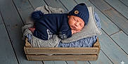 Malone is registered to the contest to win money with this photo: newborn, baby, sleeping, knitwear, hat, pom_pom, blanket, wooden_crate, floor, cozy, soft, blue, gray, cute, infant, portrait, indoors, resting, peaceful, child