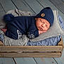 newborn, baby, sleeping, knitwear, hat, pom_pom, blanket, wooden_crate, floor, cozy, soft, blue, gray, cute, infant, portrait, indoors, resting, peaceful, child
