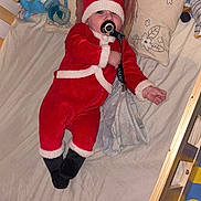 Tiago participe au concours pour gagner de l'argent avec cette photo : baby, crib, pacifier, blanket, stuffed_animals, pillow, lion_king, red_outfit, santa_costume, wooden_furniture, child, indoor, toy, bed, sleepwear, infant, cute, colorful, playful, smiling