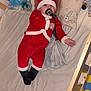 baby, crib, pacifier, blanket, stuffed_animals, pillow, lion_king, red_outfit, santa_costume, wooden_furniture, child, indoor, toy, bed, sleepwear, infant, cute, colorful, playful, smiling