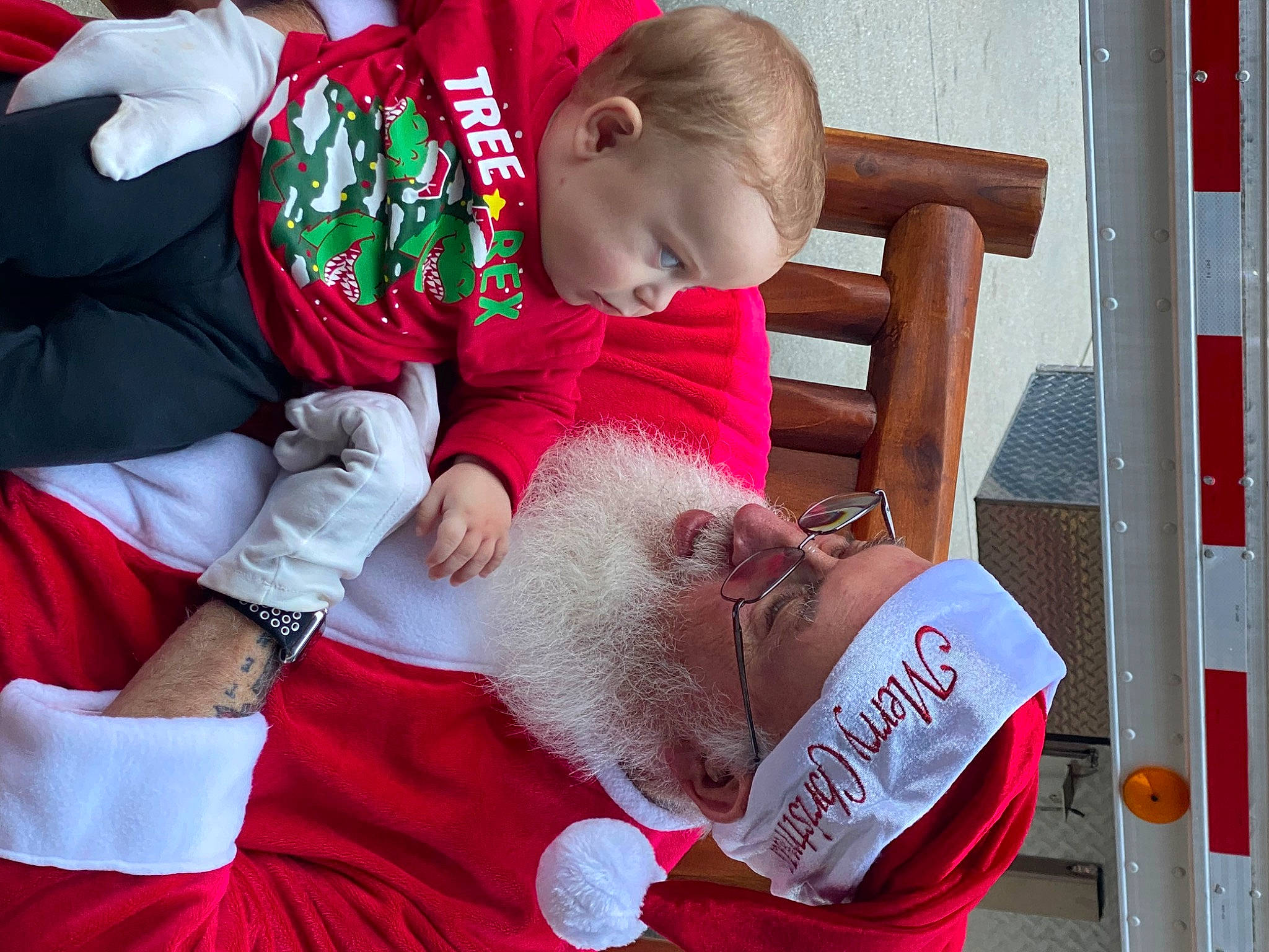 River is registered to the contest to win money with this photo: baby, beard, carmine, child, comfort, event, eyewear, fun, gesture, happy, headwear, holiday, lap, leisure, person, red, sharing, sitting, t_shirt, toddler