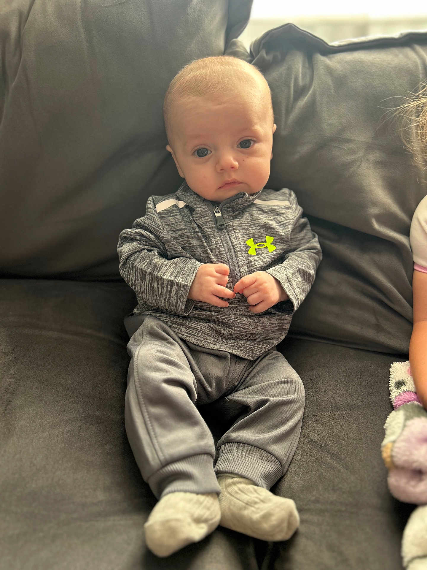 Thomas joined the competition — help win amazing prizes! baby, infant, child, sitting, couch, gray_clothing, socks, indoor, portrait, young_child, zip_up_jacket, neon_logo, cute, small_hands, looking_at_camera, soft_lighting, casual_clothing, relaxed, home, cozy