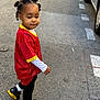 Elyjah a rejoint le concours — aidez-le/la à gagner de superbes lots ! child, toddler, street, sidewalk, sneakers, red_shirt, yellow_trim, curly_hair, hair_buns, earrings, looking_back, casual_clothing, urban, daytime, pavement, parked_car, asphalt, pose, expression, walking