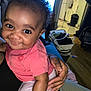 baby, child, smiling, curly_hair, indoor, person, hand, clothing, pink_shirt, white_pants, living_room, kitchen, furniture, basket, floor, home, holding, cute, happy, face