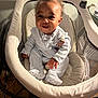 baby, infant, smile, happy, baby_rocker, clothing, white_outfit, hand, face, curly_hair, indoors, wooden_floor, baby_girl, toy_clip, footed_pajamas, child, person, home, cute, seated