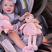 Blakely is registered to the contest to win money with this photo: baby, child, car_seat, doll, toy, pink, bow, smile, blue_eyes, footwear, seatbelt, car_interior, cute, infant, clothing, safety, happy, person, portrait, sitting