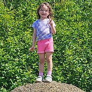 Isabella is registered to the contest to win money with this photo: child, smiling, peace_sign, standing, outdoor, greenery, gravel, shorts, tshirt, shoes, socks, nature, sunny, happy, young, portrait, summer, casual_clothing, daylight, playful