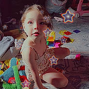 Isabella is registered to the contest to win money with this photo: carpet, casual_clothing, child, colorful, cute, daylight, expression, floor, girl, home, indoor, pattern, playroom, playtime, sitting, soft_toys, star_effect, sunlight, toy, young_child