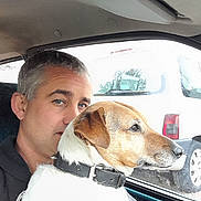 Sébastien Lamare a rejoint le concours — aidez-le/la à gagner de superbes lots ! man, dog, car, window, collar, seat, side_view, vehicle, pet, looking_out, gray_hair, short_hair, white_dog, brown_dog, black_collar, daylight, outdoor_view, parked_car, portrait, close_up