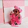 accessories, adorable, baby, child, cute, fashion, headband, indoor, infant, person, pink_robe, pink_wall, playful, portrait, sitting, soft_texture, strawberry_shaped_glasses, sunglasses, tufted_wall, white_surface