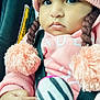 baby, child, pink_hat, pom_poms, car_seat, toy, striped_toy, hand, clothing, face, cute, infant, warm_clothing, braids, portrait, indoors, seatbelt, soft_toy, curious, close_up