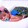 Laya is registered to the contest to win money with this photo: newborn, baby, sleeping, pacifier, headband, pink_bow, peacock_feathers, blue_flower, soft_blanket, infant, cute, portrait, closeup, peaceful, resting, skin, hand, lying_down, indoors, baby_accessory