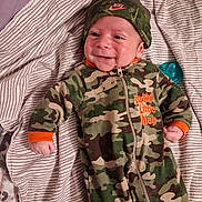 Jeremiah joined the competition — help win amazing prizes! newborn, baby, infant, child, smiling, face, portrait, lying_down, blanket, striped_blanket, camouflage, outfit, hat, clothing, pacifier, bed, indoors, happy, close_up, photography