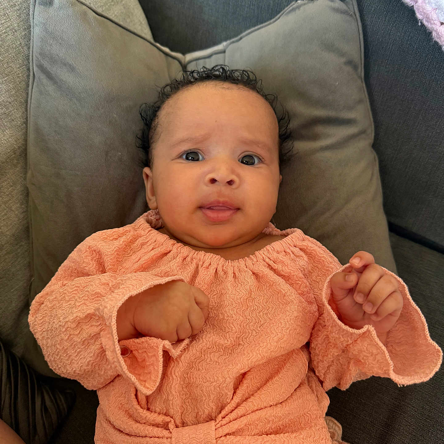 Alizaleah is registered to the contest to win money with this photo: baby, bow, child, clothing, couch, cozy, curly_hair, cute, expression, face, furniture, hand, indoors, infant, peach_outfit, person, pillow, portrait, sitting, texture