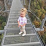 Azélïa a rejoint le concours — aidez-le/la à gagner de superbes lots ! child, girl, blonde_hair, curly_hair, smiling, white_shoes, floral_shirt, pants, suspension_bridge, metal_bridge, outdoor, nature, forest, trees, canyon, daylight, holding_object, safety_net, happy, standing