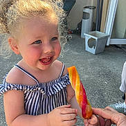 Azélïa a rejoint le concours — aidez-le/la à gagner de superbes lots ! toddler, child, smiling, outdoor, curly_hair, blue_eyes, popsicle, hand, striped_top, pink_shorts, happy, summer, sunlight, person, food, snack, fun, cute, joy, playful
