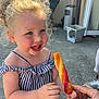 toddler, child, smiling, outdoor, curly_hair, blue_eyes, popsicle, hand, striped_top, pink_shorts, happy, summer, sunlight, person, food, snack, fun, cute, joy, playful