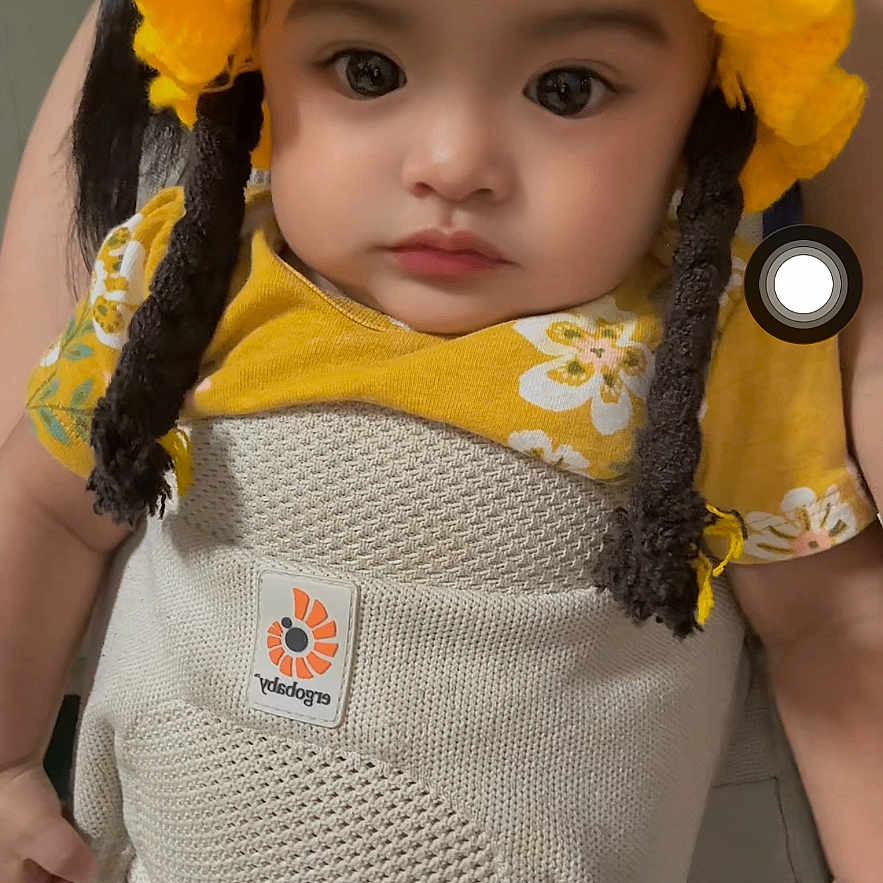 Cathriel is registered to the contest to win money with this photo: baby, child, yellow_hat, knitted_hat, baby_carrier, floral_shirt, indoor, portrait, person, cute, infant, face, clothing, young_child, closeup, human, expression, headwear, sitting, looking