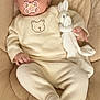 baby, child, pacifier, bow, plush_toy, bunny, cushion, clothing, onesie, footed_pants, infant, seat, beige, cute, portrait, indoor, soft_toy, smiling, relaxed, small_hands