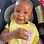 baby, smiling, child, car_seat, yellow_bib, pink_bow, happy, face, portrait, indoor, clothing, seatbelt, cute, infant, hand, embroidery, person, toddler, hair, seat