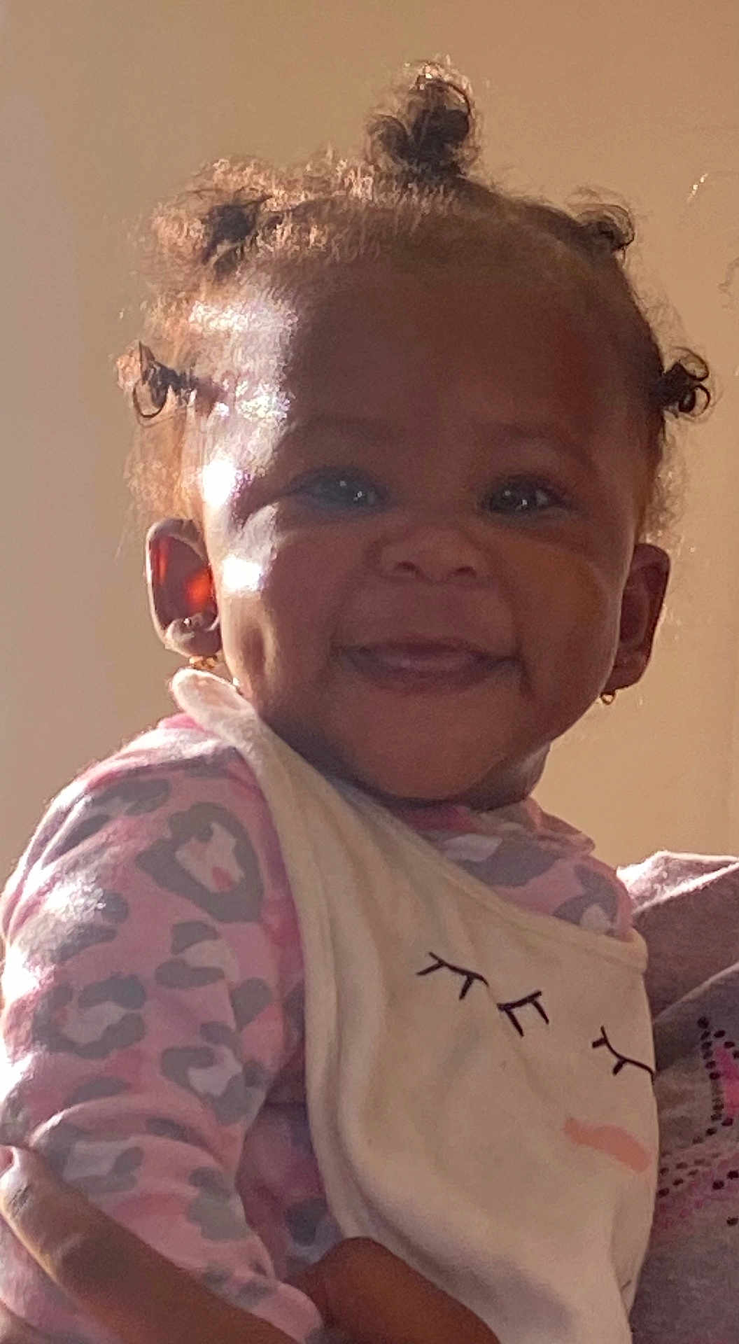Makiyha is registered to the contest to win money with this photo: toddler, child, smile, dimples, hair_buns, onesie, bib, cute, happy, face, portrait, indoor, person, baby, apparel, earrings, light, shadow, skin, expression