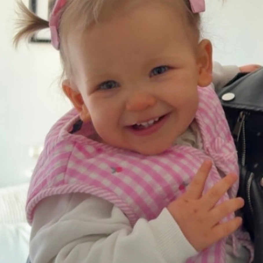 Victoire a rejoint le concours — aidez-le/la à gagner de superbes lots ! toddler, child, smiling, pink_bib, pigtails, white_sweater, indoor, portrait, happy, baby, face, person, home, furniture, couch, hair_bow, cute, hand, young_child, infant