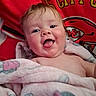 baby, child, blanket, pink_blanket, tongue_out, happy, smiling, face, chubby_cheeks, red_background, sports_logo, kc_chiefs, infant, portrait, cute, wrapped, indoors, young_child, soft_texture, closeup