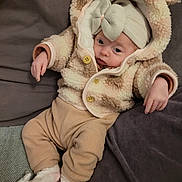 Sofia participe au concours pour gagner de l'argent avec cette photo : baby, child, infant, hooded_jacket, bear_ears, bow_hat, unicorn_slippers, couch, cushion, cozy_clothing, soft_fabric, relaxed, indoors, person, cute, warm, sleepwear, pink, beige, comfortable