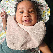 Sarai joined the competition — help win amazing prizes! baby, smiling, infant, pink_bib, floral_blanket, curly_hair, raised_fist, tongue_out, cute, child, portrait, closeup, lying_down, happy, face, clothing, indoors, skin, person, young