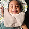 baby, smiling, infant, pink_bib, floral_blanket, curly_hair, raised_fist, tongue_out, cute, child, portrait, closeup, lying_down, happy, face, clothing, indoors, skin, person, young