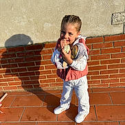 Maëlane a rejoint le concours — aidez-le/la à gagner de superbes lots ! braided_hair, brick_wall, casual_clothing, child, daylight, doll, girl, happy, outdoor, pink_vest, plaster_wall, playful, portrait, shadow, smiling, standing, sunlight, toy, white_pants, white_shoes
