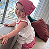 Elyanna is registered to the contest to win money with this photo: child, toddler, baby, portrait, smiling, indoors, sofa, cushion, window, cityscape, water, sky, daylight, dress, headscarf, red_and_white, standing, fashion, home, happy