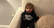 Elyanna joined the competition — help win amazing prizes! armchair, baby, black_clothing, blinds, brown_hair, child, couch, curtains, face, fluffy_pillow, home, indoors, pillow, portrait, sitting, sweatshirt, toddler, warm_lighting, white_socks, window